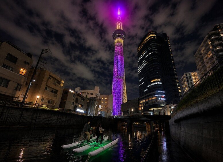 A nighttime cityscape with a brightly lit tower and a river with boats. 2