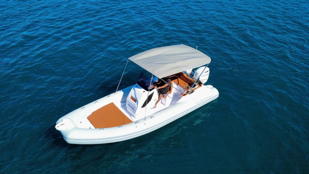 A white motorboat with a canopy and two passengers on the water. 3