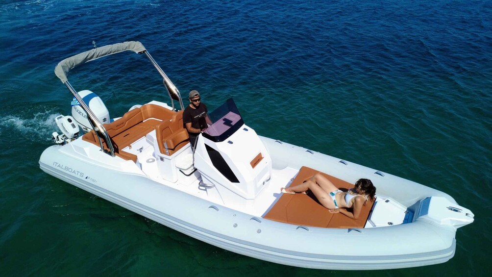 A white motorboat with two people on board, one standing and one lying down, on a body of water. 1