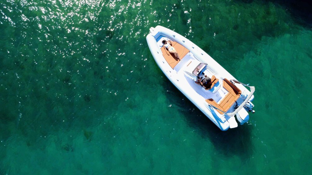 A small inflatable boat with a wooden deck and seating, floating on clear green water. 4