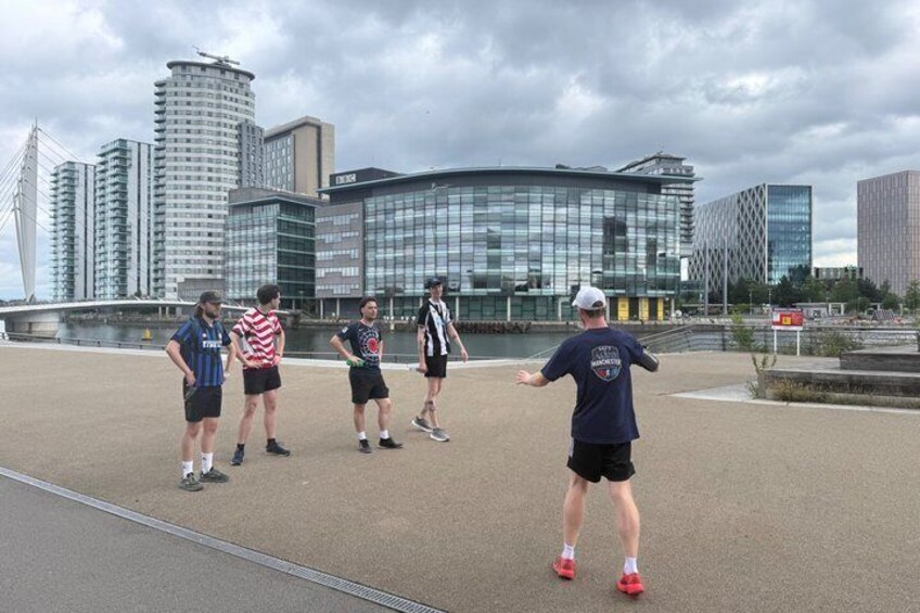 A group of people on a sports field with a modern building and a bridge in the background. 3