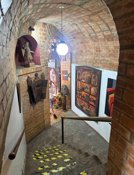 A brick-walled corridor with a staircase, a statue, and various artworks. 2