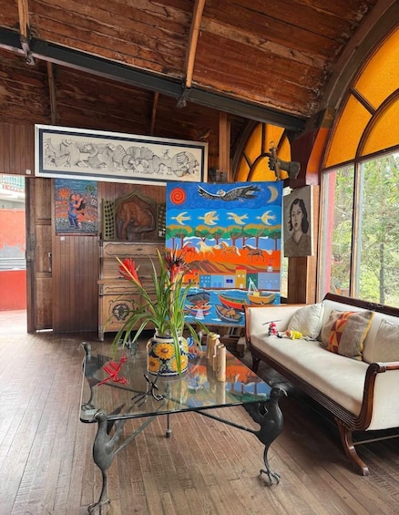 A room with wooden walls, a glass coffee table, a sofa, and colorful paintings. 1