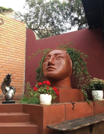 A sculpture of a human head with a brick wall and potted plants in the background. 3
