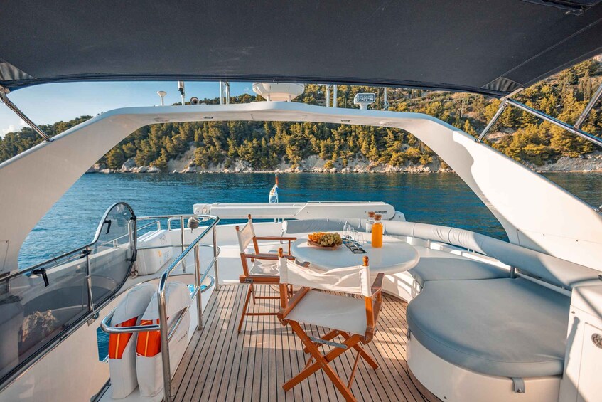 A boat deck with a table, chairs, and a view of a calm sea and a forested coastline. 3