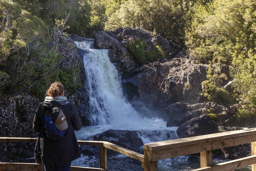 A person standing on a wooden bridge overlooking a waterfall in a forested area. 4