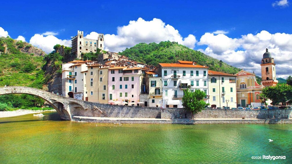 A historic town with a stone bridge over a river, colorful buildings, and a church with a bell tower. 2