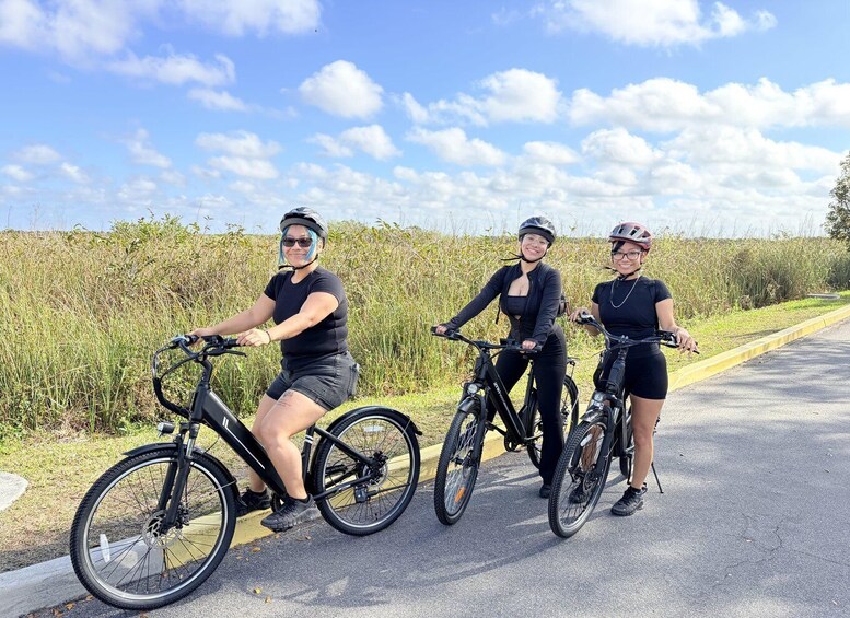 Three people on bicycles on a road with grass on the sides. 1