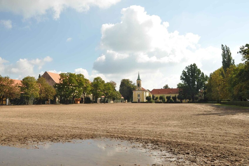 A large open field with a church and residential buildings in the background. 1