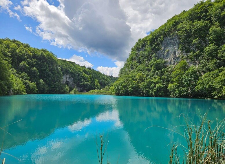 A turquoise lake surrounded by lush green hills and a cloudy sky. 5