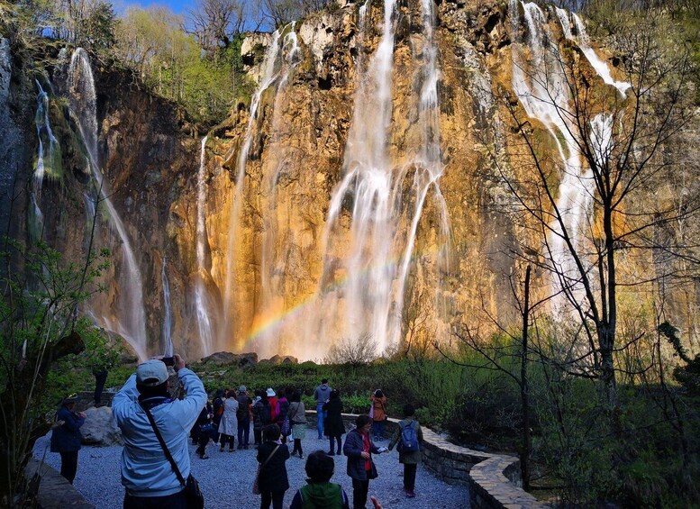 A waterfall with a rainbow, surrounded by visitors. 1