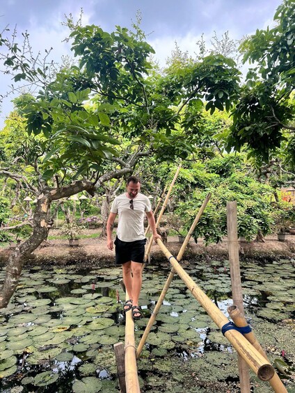 A person walking on a bamboo bridge over a pond with lily pads. 4