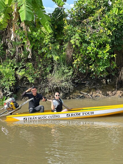 A yellow boat with 'TRAN QUOC CUONG' and 'ROM TOUR' written on it, floating on a river surrounded by dense greenery. 3
