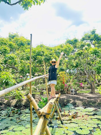A person balancing on a bamboo bridge over a pond with lily pads. 5