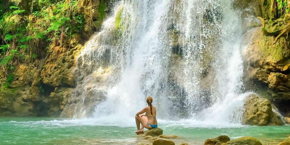 A waterfall with a person sitting on rocks in the foreground. 5