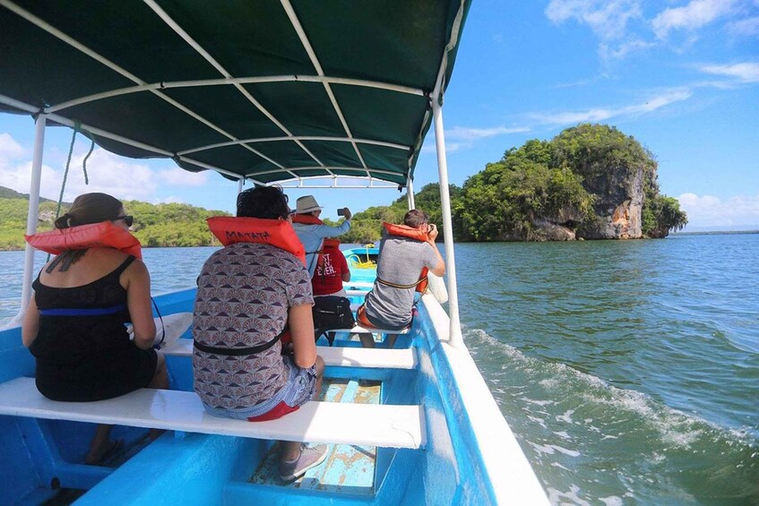 A boat with passengers wearing life jackets, moving towards a green island with dense vegetation. 2