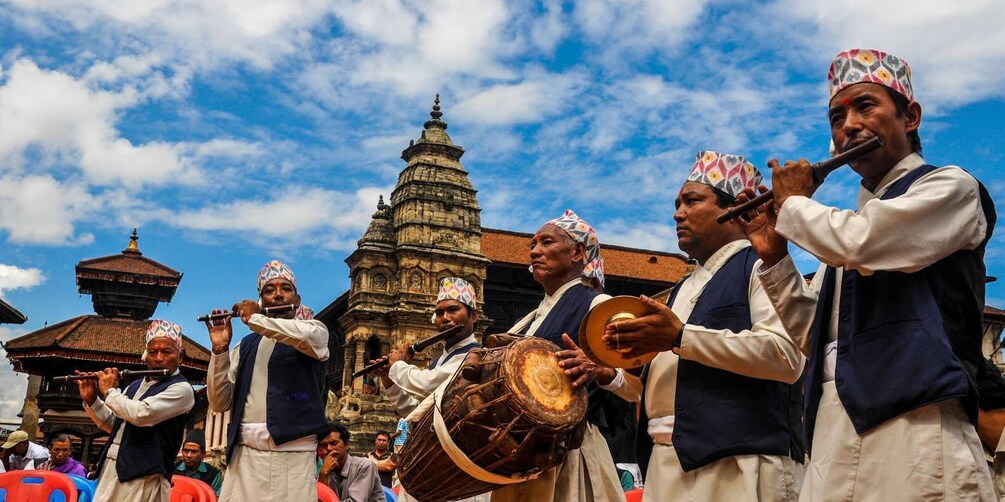 A group of musicians performing outdoors with traditional instruments, a historic building, and a clear sky in the background. 3
