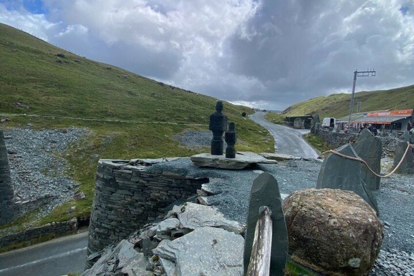 A stone wall, a large boulder, and a road leading to a building with a red roof. 4