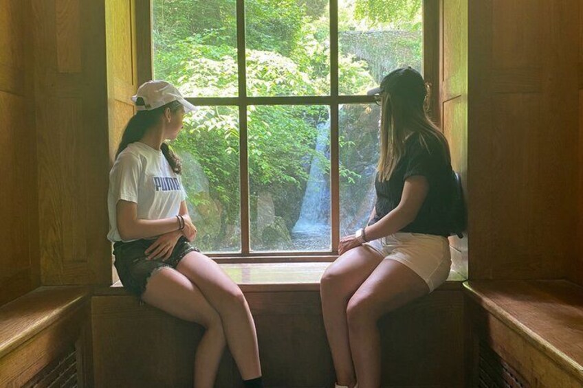 Two people sitting on a bench by a window with a view of greenery. 2