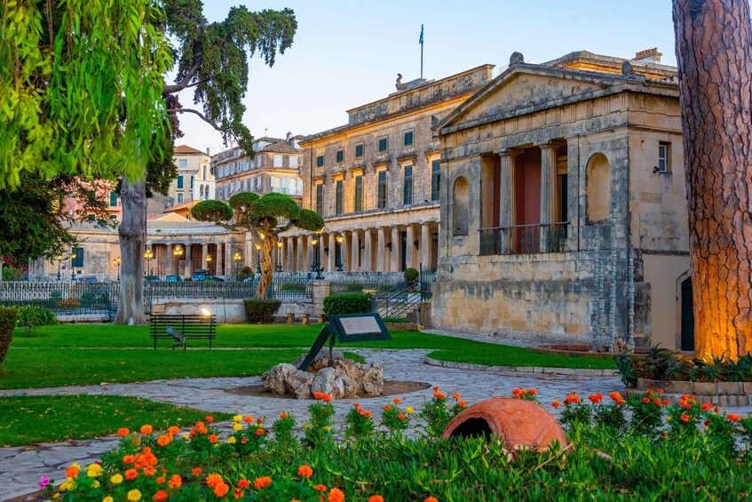 A historic building with columns, a fountain, and a well-maintained garden with flowers. 4