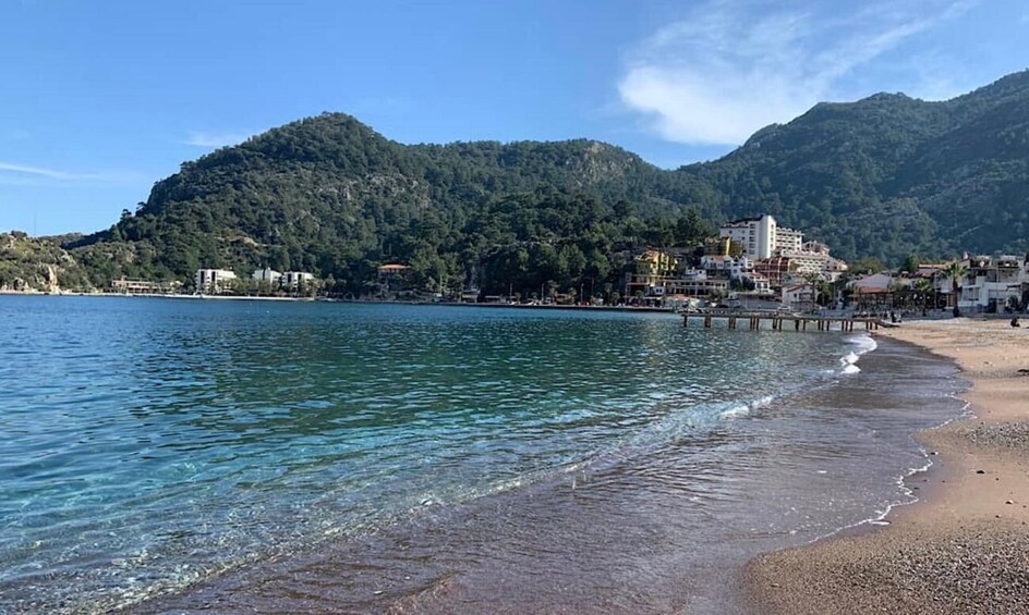 A coastal beach with clear waters, a sandy shore, and a backdrop of green hills. 5