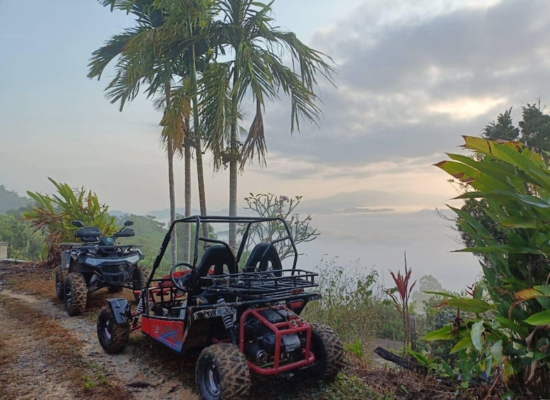 Two off-road vehicles parked on a dirt path with palm trees and tropical vegetation in the background. 1