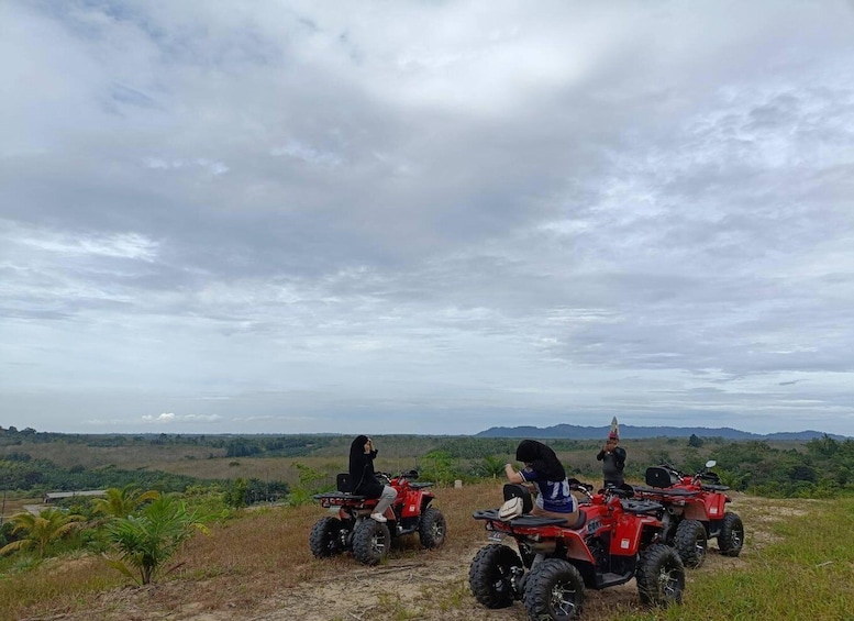 Three people on red ATVs in a rural landscape with hills and palm trees. 5