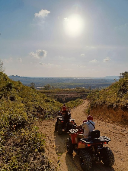 Two people riding ATVs on a dirt path with a scenic landscape in the background. 3