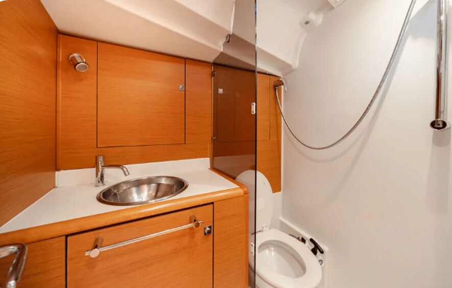 A compact bathroom with a stainless steel sink, wooden cabinets, and a toilet. 3