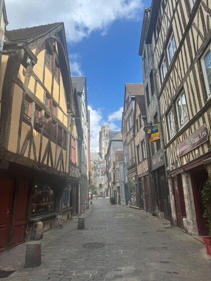 A cobblestone street lined with half-timbered buildings, a church spire in the distance, and a sign for 'Restaurant des Beaux Arts'. 2