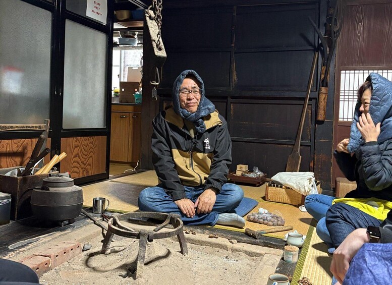 Two people sitting on the floor in a rustic setting with cooking utensils and a traditional stove. 5