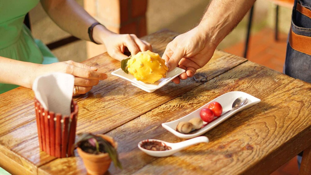 A wooden table with a plate of mango, a dish with cherry tomatoes, and a small potted plant. 1