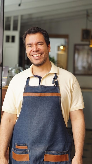 A person wearing a denim apron over a light-colored shirt, standing indoors with a blurred background. 4