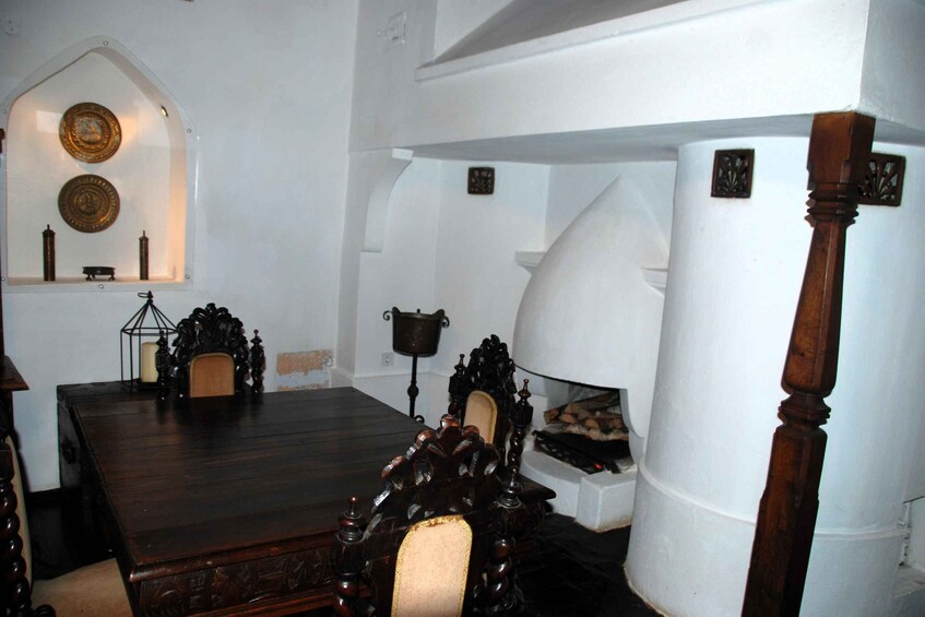 A traditional room with a wooden table, ornate chairs, a fireplace, and decorative plates on the wall. 2