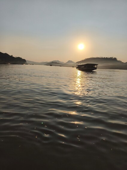 A calm lake at sunset with a boat in the foreground and mountains in the background. 1