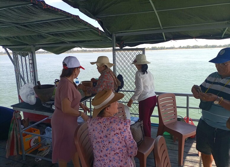 A group of people on a boat with a covered deck, some wearing hats, and a calm body of water in the background. 5