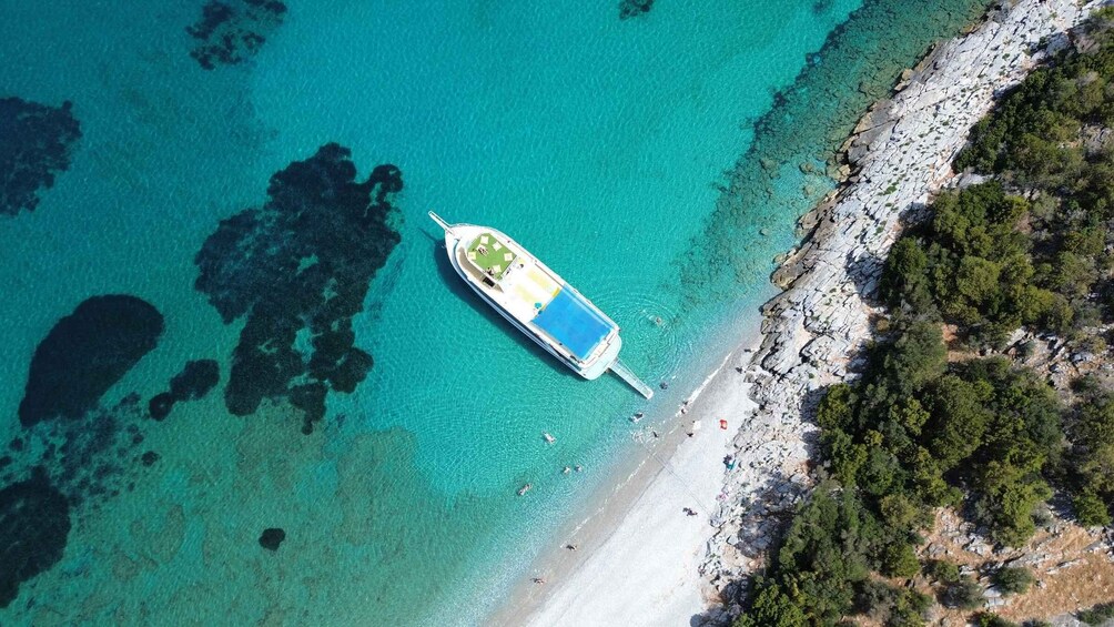 An aerial view of a boat anchored near a beach with clear turquoise water and rocky shoreline. 1