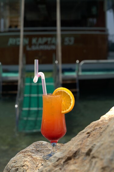 A glass of orange juice with a straw and an orange slice on a rock by a boat. 5