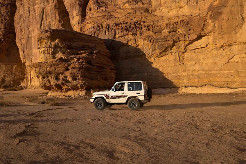 A white SUV parked on a desert road with a large rock formation in the background. 5