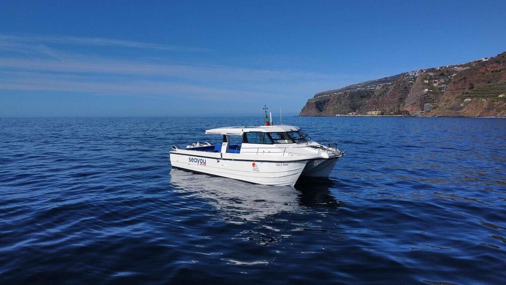 A white boat named 'seayou' on calm blue waters with a hilly coastline in the background. 3