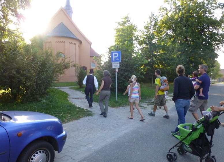 A group of people walking on a sidewalk, a church, and a parking sign. 1