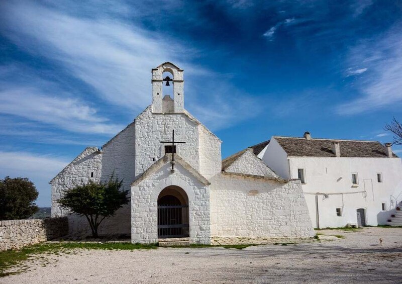 A white church with a bell tower, a stone wall, and a tree in front. 1