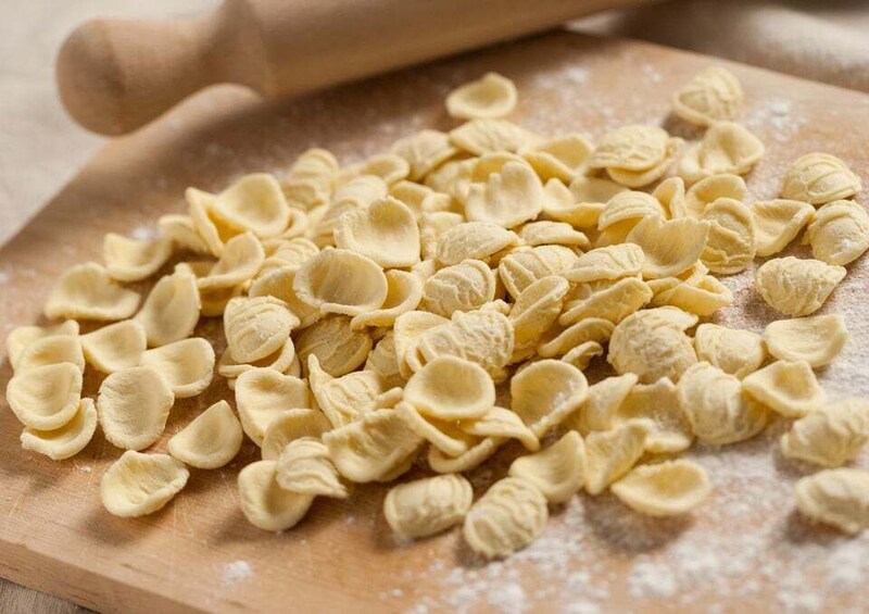 Uncooked pasta shells on a wooden surface with a rolling pin in the background. 2