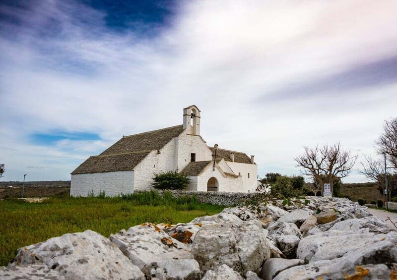 A white church with a bell tower, surrounded by rocks and grass. 3