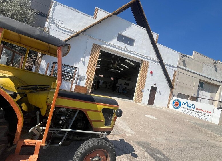 A yellow tractor parked in front of a white building with a large garage door. 1