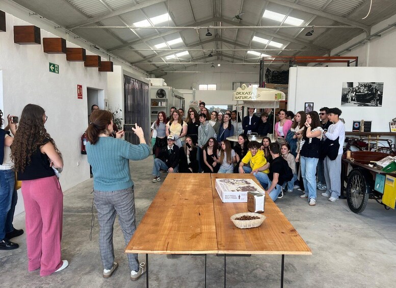 A group of people gathered around a table in an industrial setting with a wooden table, a basket of items, and a fan in the background. 5