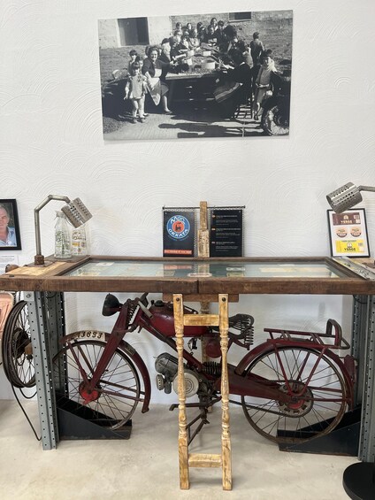 A vintage bicycle with a wooden stand, a glass display case, and a black-and-white photograph on the wall. 2