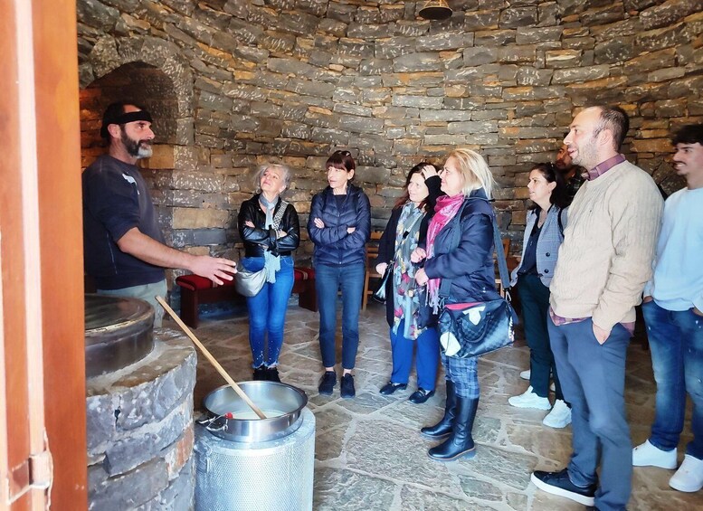 A group of people standing indoors near a stone wall and a large metal container. 4