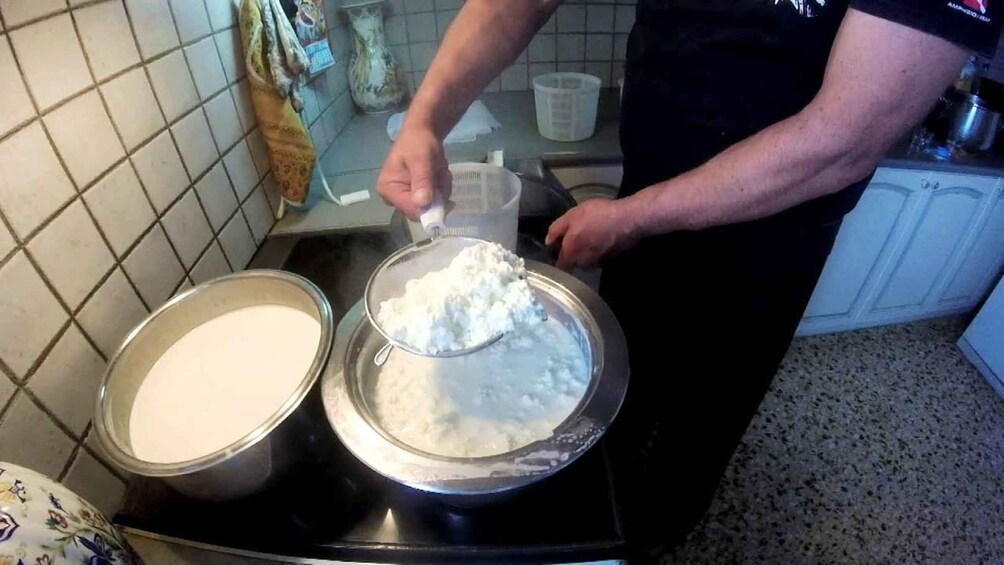A person in a kitchen preparing food, with two metal bowls on a stove, one containing a white liquid and the other a white powder. 1