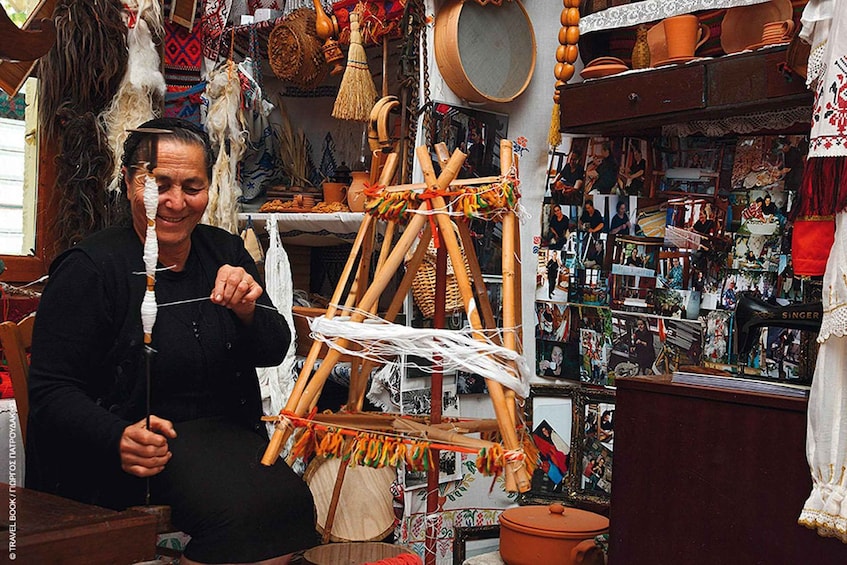 A person weaving with a loom in a room filled with various items and decorations. 1